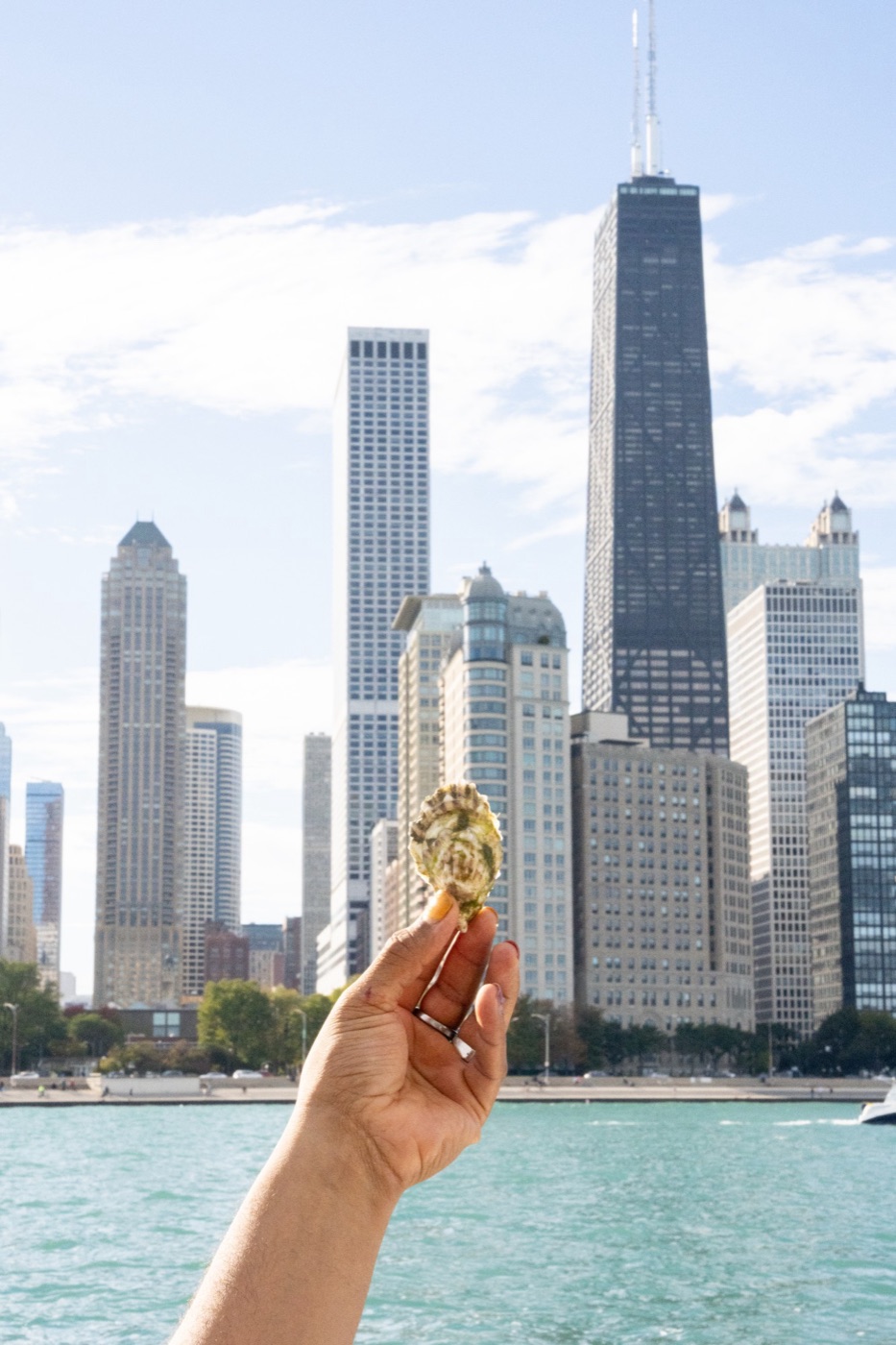 A guest holds up a freshly shucked oyster with the Chicago skyline behind